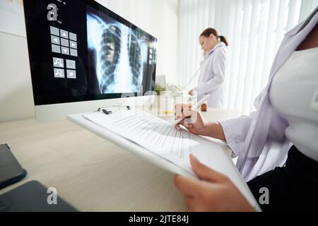 Image rognée de la radiographie pulmonaire du patient et prise de notes dans le document Banque D'Images