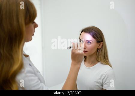 Jeune femme en nomination neurologue. Une femme médecin vérifie les réflexes des yeux avec une lampe de poche Banque D'Images