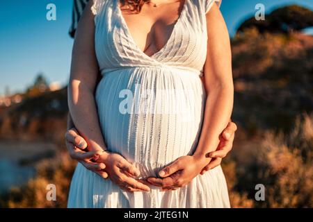 Femme enceinte avec son partenaire tenant son ventre dans la nature Banque D'Images