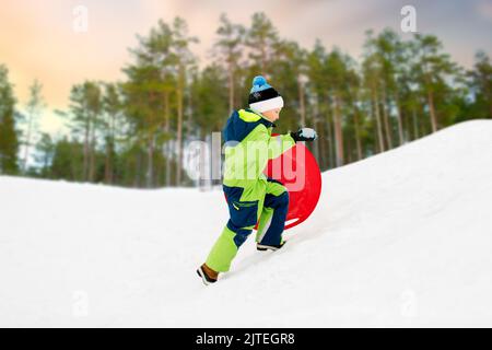 Happy boy avec de la neige en hiver luge soucoupe Banque D'Images