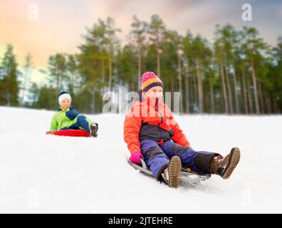 Happy kids sur des traîneaux glissant en bas de la colline en hiver Banque D'Images