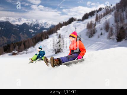 Happy kids sur des traîneaux glissant en bas de la colline en hiver Banque D'Images