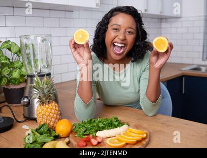 Une jeune femme multiethnique se pose avec des oranges et des rires tout en faisant du smoothie Banque D'Images