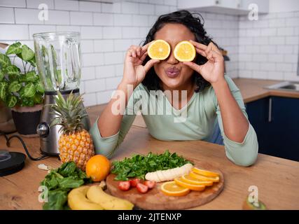 Une jeune femme multiethnique tient des oranges à ses yeux et lui porte un baiser Banque D'Images