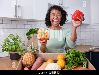 Une jeune femme végétalienne s'excite à propos des fruits frais et de la boîte de légumes dans la cuisine Banque D'Images