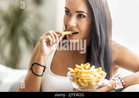 Femme mangeant un bol de frites en croquant jaune frite dans ses doigts. Banque D'Images