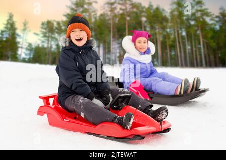 Heureux les petits enfants glissant sur les traîneaux en hiver Banque D'Images