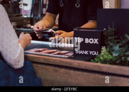 Femme d'Asie utilise Wi-Fi paywave sans espèces scanner sur le lecteur de carte dans le café. Banque D'Images