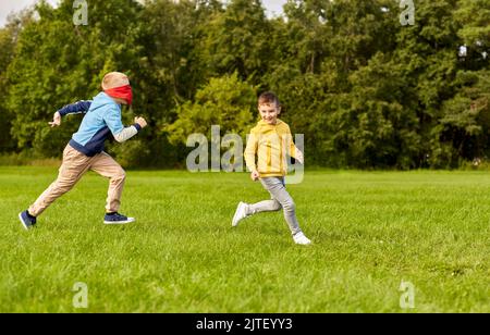 les garçons heureux jouant à la recherche et à la peau de jeu au parc Banque D'Images