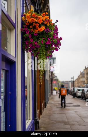 Seau à fleurs suspendu sur la rue britannique, homme de livraison de nourriture dans un arrière-plan flou. Banque D'Images