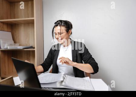 Jeune fille souriante travaillant au bureau. Heureux, joli, étudiant de race mixte regardant un écran d'ordinateur, regardant un webinaire ou une étude en ligne Banque D'Images