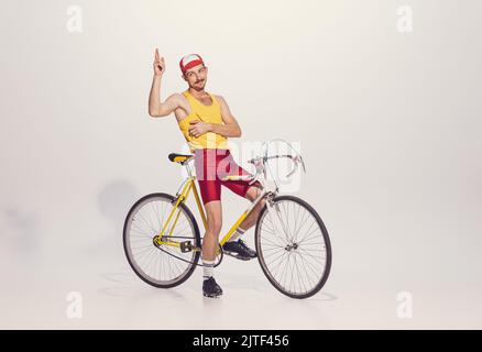 Portrait du jeune homme en vêtements colorés, vélo d'équitation uniforme isolé sur fond gris. Livreur de pizza Banque D'Images