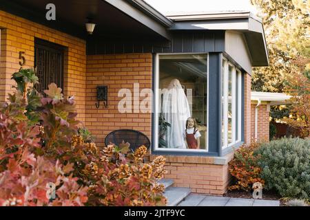 Petite fille (2-3) et père habillé comme fantôme d'Halloween debout dans la fenêtre Banque D'Images
