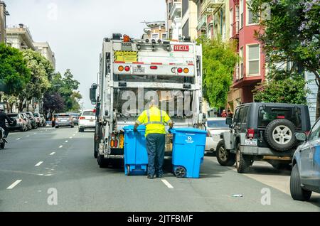 Un homme vide des poubelles à roues bleues contenant du papier de rebut à l'arrière d'un camion à ordures ou d'un camion à benne dans une rue à San Francisco, Californie, États-Unis Banque D'Images