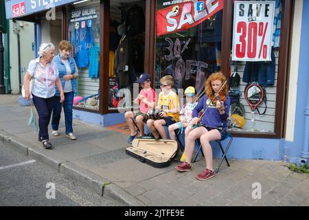 Ballycastle, Royaume-Uni. 30 août 2022. Deux femmes marchent vers quatre jeunes enfants musiciens jouant de la musique traditionnelle irlandaise dans la rue, le jour de clôture de la plus ancienne foire d'Irlande dans la ville balnéaire de Ballycastle sur la côte nord d'Antrim, terminant un week-end de commerce de vacances, et un programme rempli de divertissement, de cuisine locale et internationale à la foire Ould Lammas. Crédit : Steve Nimmons/Alamy Live News Banque D'Images