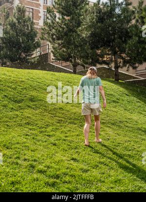 Bonne jeune femme pieds nus marchant sur une pelouse d'herbe verte appréciant la pluie chaude en été appréciant la sensation de la nature Banque D'Images