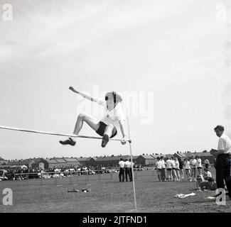 1960s, historique, sports d'école de comté, un garçon faisant le saut élevé, les pieds d'abord, dans une technique de saut de type ciseaux, Écosse, Royaume-Uni. Banque D'Images