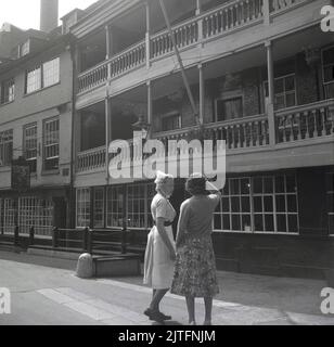 1963, historique, une dame et une infirmière debout à l'extérieur de la taverne historique, le George Inn, situé à la sortie de Borough High Street à Southwark, Londres, Angleterre, Royaume-Uni. Guy's Hospital, un grand hôpital NHS est à proximité. La célèbre maison publique, le George Inn est la seule auberge de coaché survivante à Londres. Banque D'Images