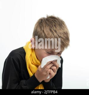 Un enfant souffle son nez dans une serviette, les maladies saisonnières des enfants, un garçon enveloppé dans un foulard, les symptômes de la maladie. Banque D'Images