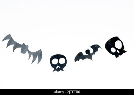 Crânes et chauves-souris volantes coupées de papier noir sur fond blanc, préparation pour les vacances d'Halloween, isolées sur fond blanc. Banque D'Images