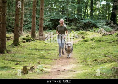 Portrait d'une jeune femme qui court avec un chien de Laponie finlandais dans la forêt ou les bois Banque D'Images