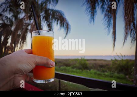 Main tenant un verre de jus d'orange sur les rives d'une rivière Banque D'Images