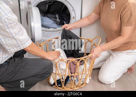 Couple senior travaillant ensemble pour compléter leurs tâches ménagères à la machine à laver de manière heureuse et agréable. Mari et femme faisant le Banque D'Images