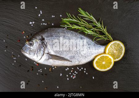 Poisson cru dorado sur fond d'ardoise noire avec épices, romarin et citron. Vue de dessus, plan d'affichage avec espace de copie pour le texte Banque D'Images