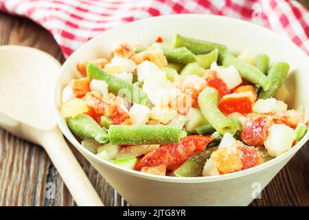 Un mélange de légumes surgelés assortis dans un bol blanc prêt à cuire sur une table en bois brun. Flat lay, vue de dessus Banque D'Images