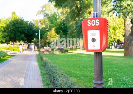 SOS, police, bouton d'urgence dans le parc public. Boîtier rouge avec caméra vidéo et voyant d'avertissement bleu sur le dessus Banque D'Images