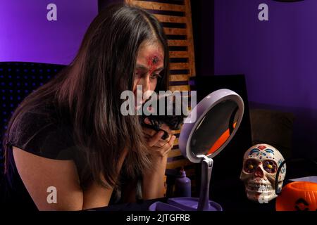 Adolescente regardant son halloween horreur maquillage dans le miroir avec son chiot chat noir Banque D'Images