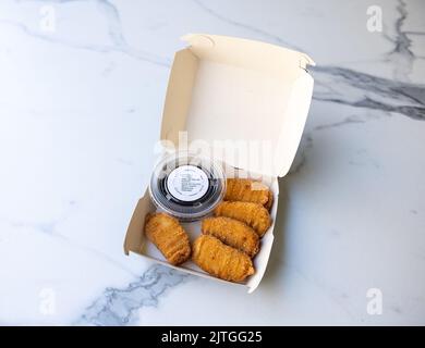 Une boîte en papier avec sauce et nuggets de poulet sur une table en marbre Banque D'Images