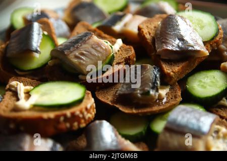 Refocalisation du sandwich avec du hareng et du concombre. Un morceau de pain noir. Une alimentation saine. Assiette de sandwiches avec poisson frais de hareng sur fond sombre. Clos Banque D'Images