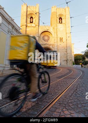 La Cathédrale Saint Mary Major alias la Cathédrale de Lisbonne (Sé de Lisboa). Tram et un cycliste de livraison avec un sac jaune à l'avant. Soirée de Summers. Banque D'Images