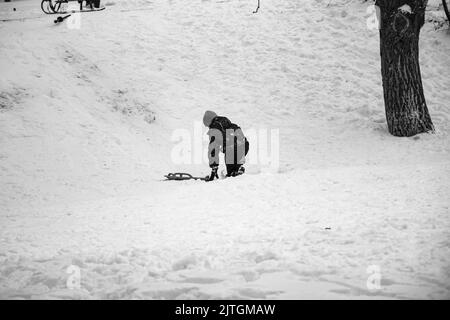 Un petit garçon s'est traîné en descente en hiver. Le garçon tombe dans la neige. Jeux en plein air pour les enfants. Des luges pour enfants dans un parc couvert de neige. Enfance, Banque D'Images