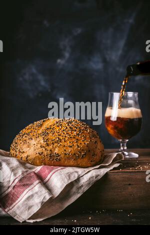 Pain rond de poppyseed pain avec bière foncée dans le verre et la bière verser action Banque D'Images