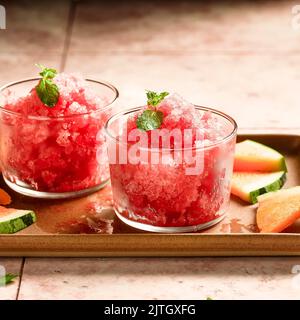 Petites tasses de granita de pastèque sur un plateau avec des cuillères et des tranches de pastèque d'orange. Banque D'Images