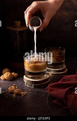 Verser du lait dans un café glacé sur un fond sombre Banque D'Images