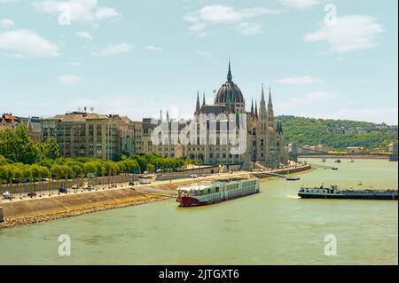 Vue sur le paysage du Parlement à Budapest, Hongrie, avec le Danube et de longs bateaux en premier plan traversant le fleuve. Banque D'Images