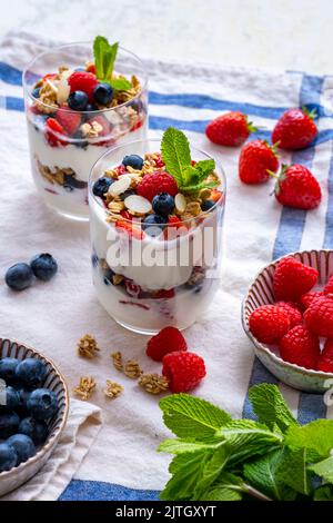 Yaourt et parfait aux fruits servis dans deux verres et accompagnés de fraises, de bleuets, de framboises et de feuilles de menthe fraîche. Banque D'Images