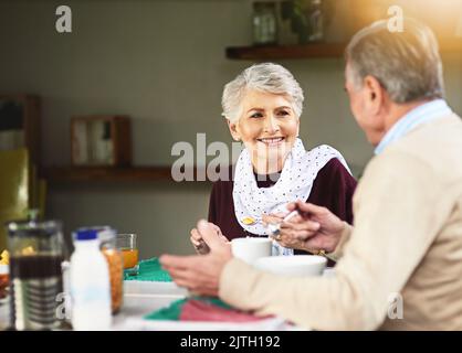 Commencez votre journée par une entreprise de personnes aimées. Un couple de personnes âgées heureux prenant le petit déjeuner ensemble à la maison. Banque D'Images