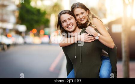 C'est tout le plaisir et les jeux quand theyre ensemble. Portrait d'un jeune couple heureux profitant d'une promenade en pigeyback dans la ville. Banque D'Images