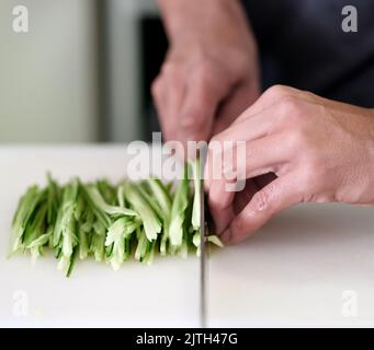 Des mains stables sont nécessaires. Un jeune homme inidentifiable coupe des légumes dans sa cuisine. Banque D'Images