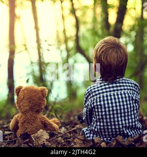 Enseigner à Teddy quelques choses sur la nature. Un petit garçon assis dans la forêt avec son ours en peluche. Banque D'Images