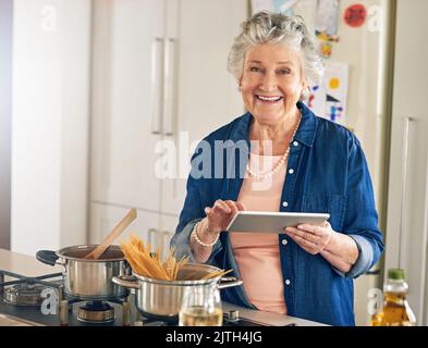 J'ai essayé une nouvelle recette que j'ai trouvée en ligne. Portrait d'une femme âgée utilisant une tablette numérique tout en cuisinant dans sa cuisine. Banque D'Images