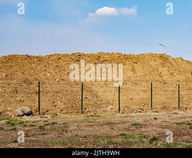 Travaux de terrassement en extérieur avec une grande pile de sable derrière la clôture et un paysage céleste. Banque D'Images