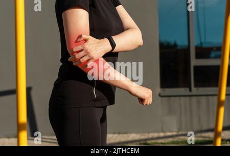 Femme faisant du sport et souffrant de douleurs au coude. Femme tenant un bras douloureux avec point rouge pendant l'entraînement à l'extérieur. Conséquences des blessures. Haute qualité Banque D'Images