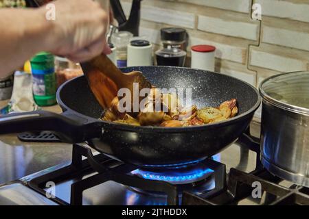 Le chef agite des pommes de terre en tranches de champignons sur une poêle à gaz Banque D'Images