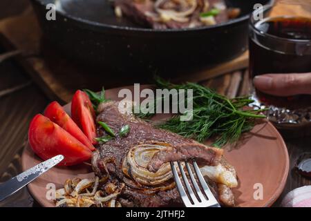 la main féminine tient le verre avec de la bière foncée.morceau de boeuf marbré grillé broché sur la fourchette, se concentre sur la viande.poêle avec le boeuf entier steak brouillé.nourriture saine co Banque D'Images