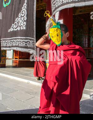 Jeune moine bouddhiste tibétain débutant portant des robes rouges , accueillant les visiteurs au monastère de Litang en Chine en portant un masque maison. Banque D'Images